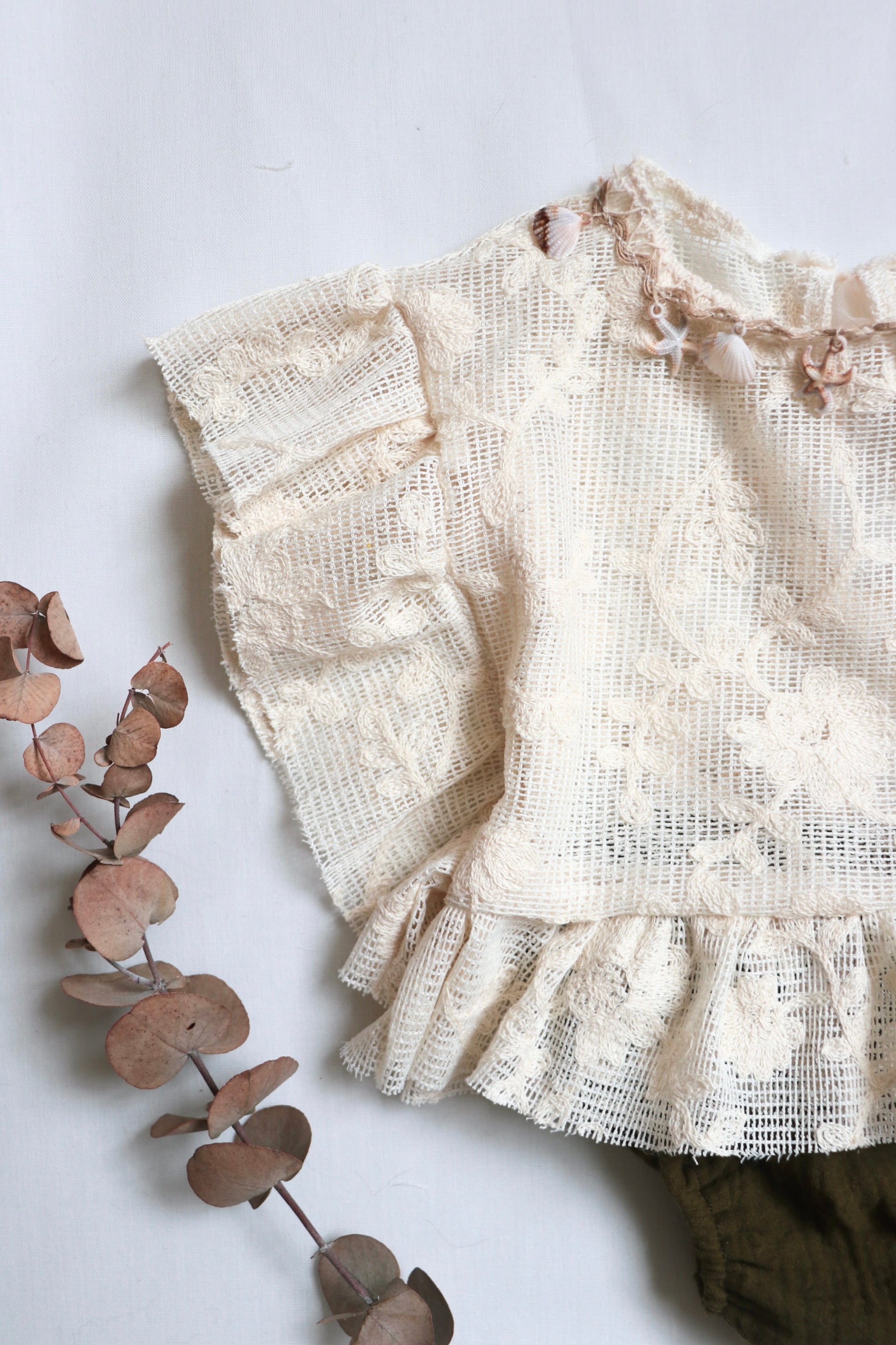 "Close-up of a baby outfit featuring a soft ruffled top with lace and shell accents, styled with a sapin green bloomer for a dreamy boho photo shoot."