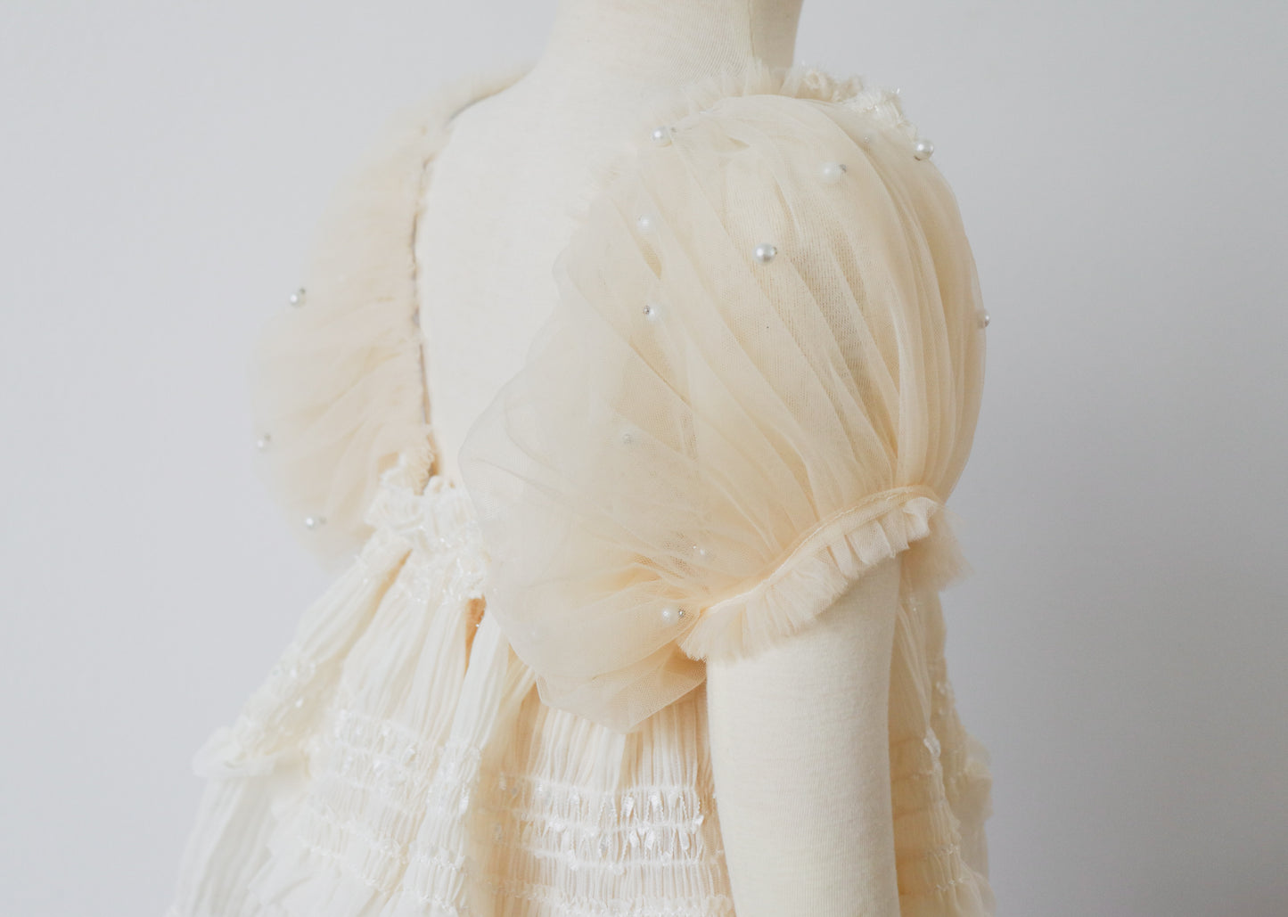 Close-up of baby romper with delicate pearl ruffles and ivory chiffon overlay, ideal for baby’s special celebration.