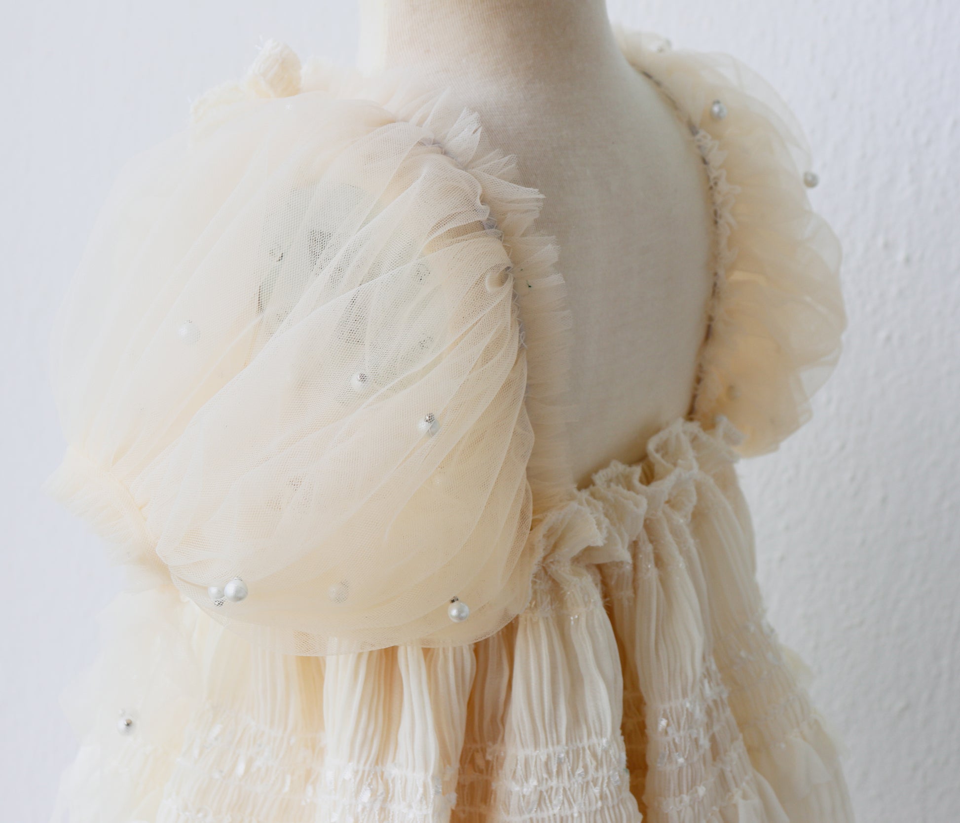 Baby girl dressed in a soft ivory romper with pearl accents, captured during a dreamy outdoor photo se