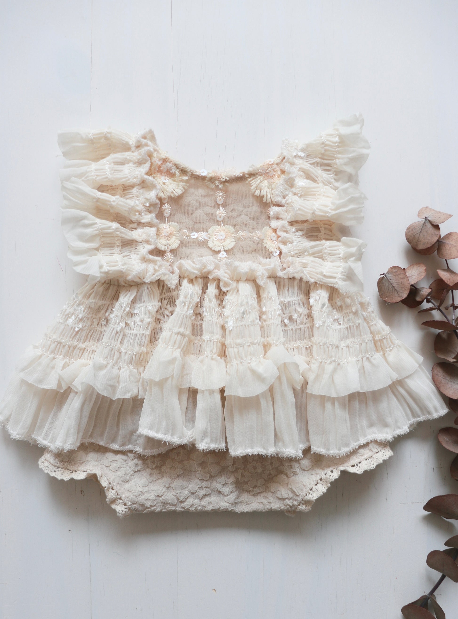 Newborn girl romper dress made with stretch cotton, featuring 3D beige flowers on the bodice, ruffled ivory chiffon accents on the sides, and a flowing chiffon skirt.