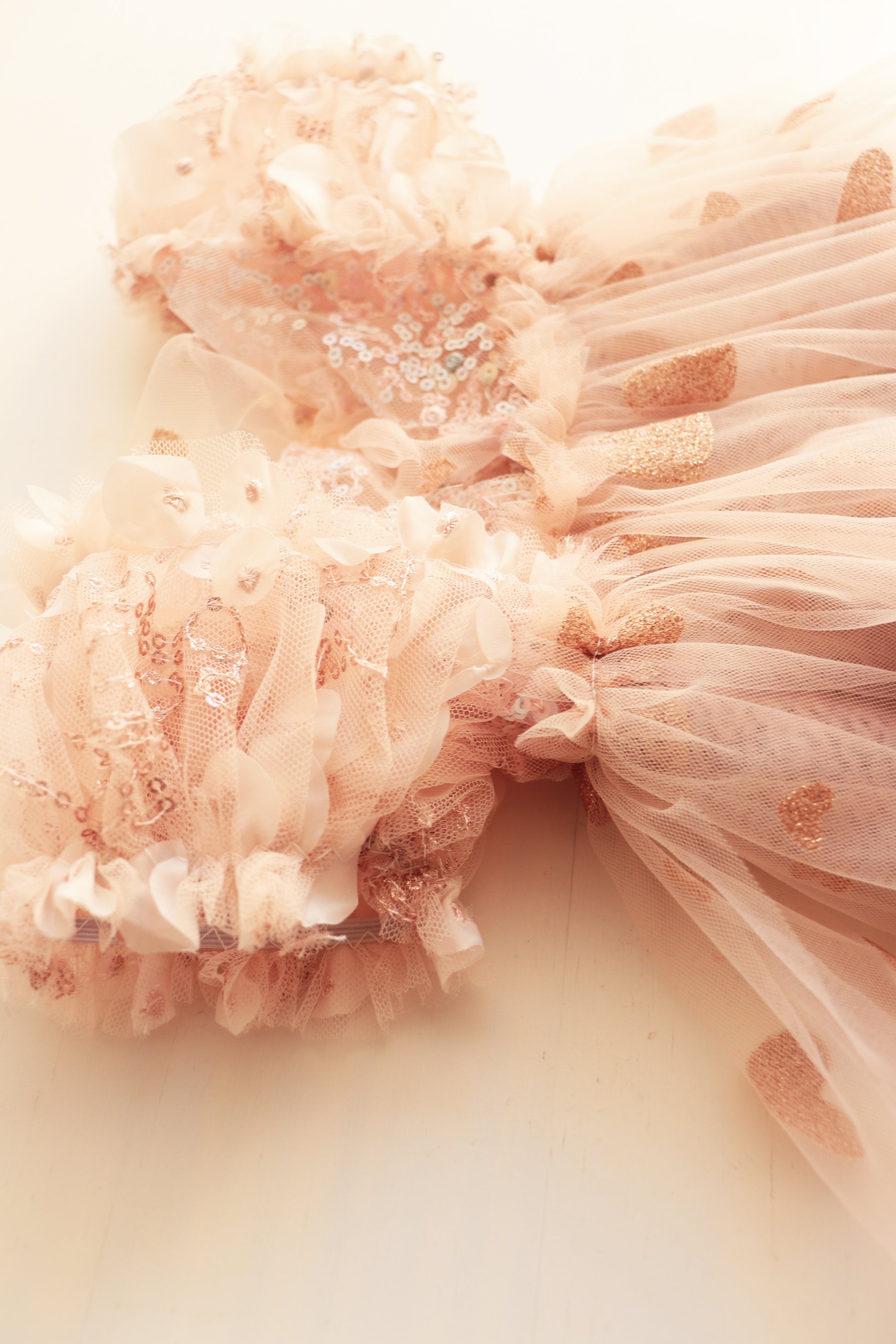 Newborn girl’s romper dress with pink puffed sleeves, sequined bodice, and soft golden tulle skirt