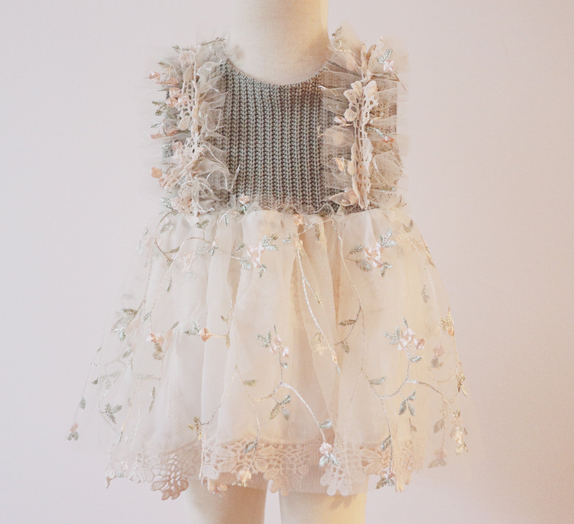 A sage green girl’s dress set featuring a soft wool bodice with peach flower embroidery on tulle, ruffled tulle sides, and a flowing chiffon skirt with vintage lace trim. Includes matching bloomers with lace details, perfect for photoshoots and special occasions."