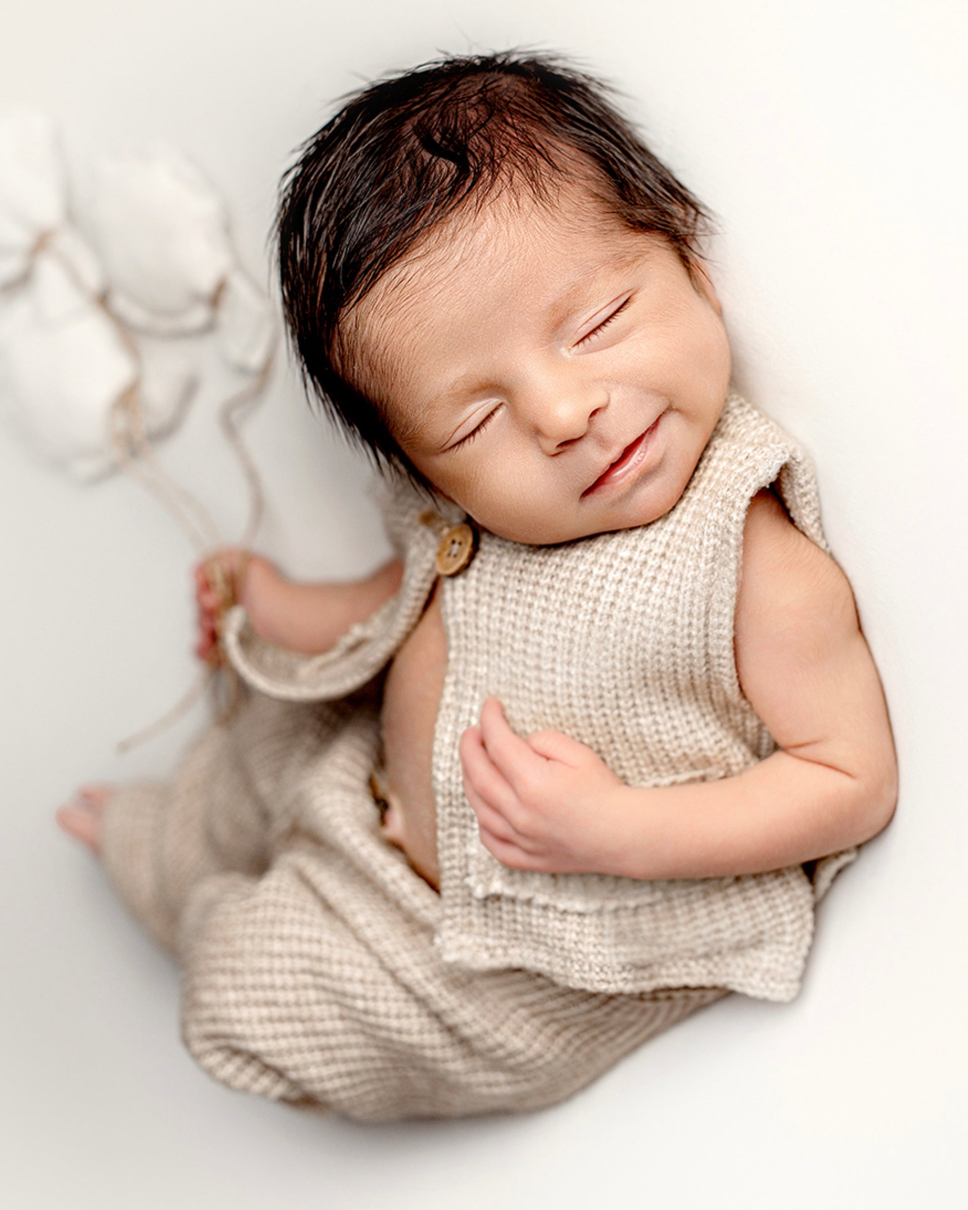 Beige newborn photo session outfit on a sleeping baby, featuring a textured vest and pants