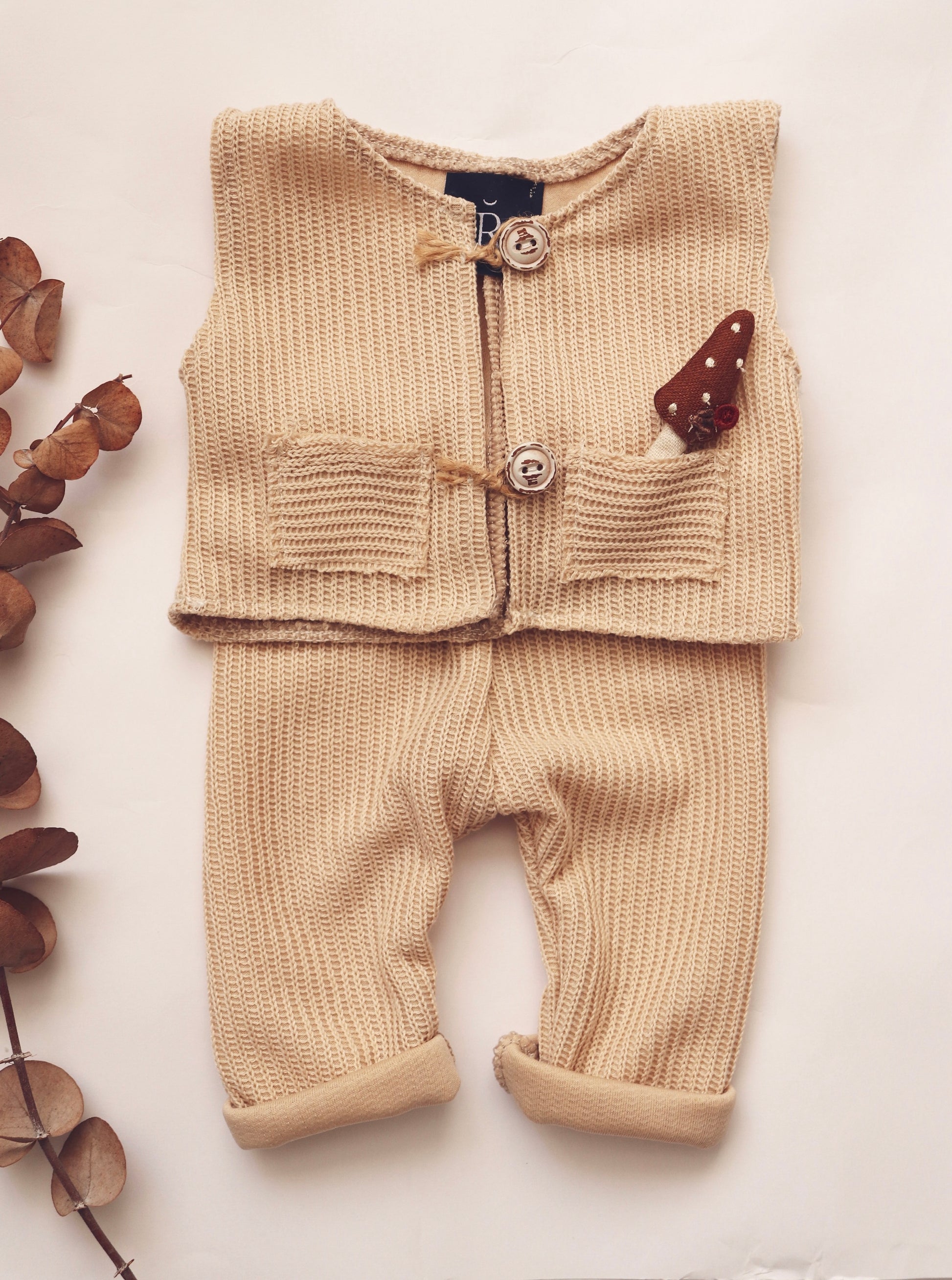 Beige newborn photo session outfit featuring a knitted vest and pants with a cute mushroom detail