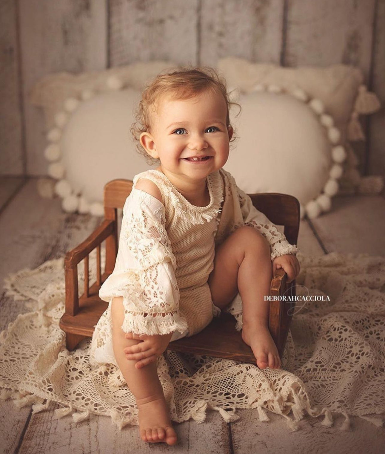 Smiling baby girl in boho girl photoshoot outfit sitting on wooden chair with crochet blanket