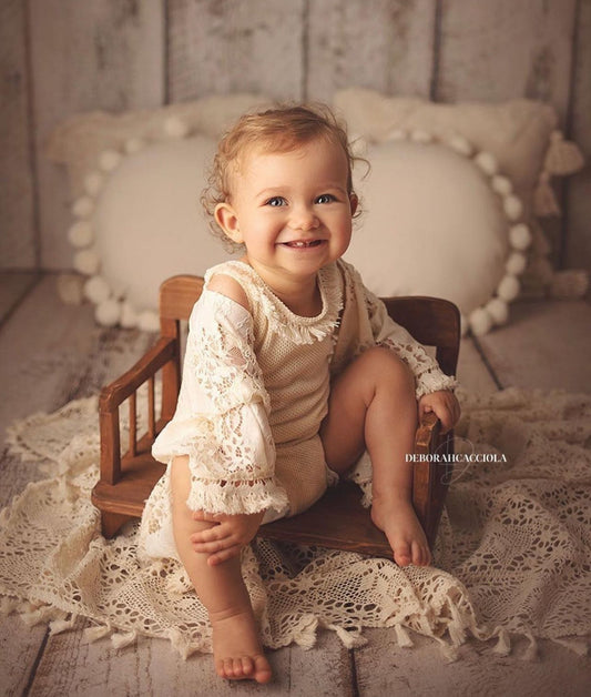 Smiling baby girl in boho girl photoshoot outfit sitting on wooden chair with crochet blanket