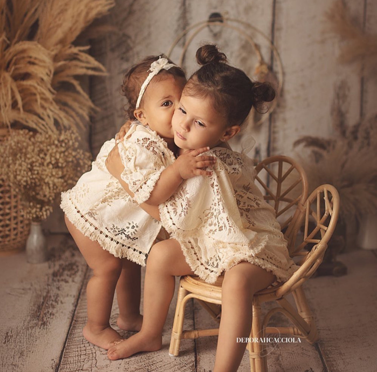 Two young girls wearing cream lace boho girl photoshoot outfit sitting and hugging in rustic setting