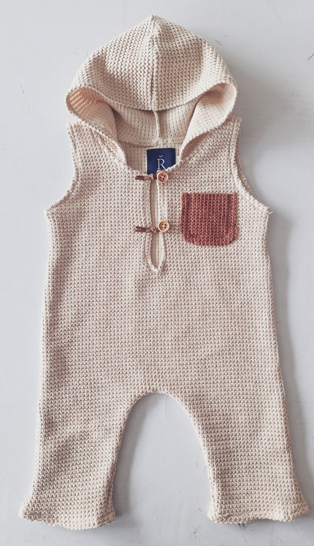 RBYFLEURMARGOT beige knitted hooded sitter romper for photoshoot with brown pocket and wooden buttons
