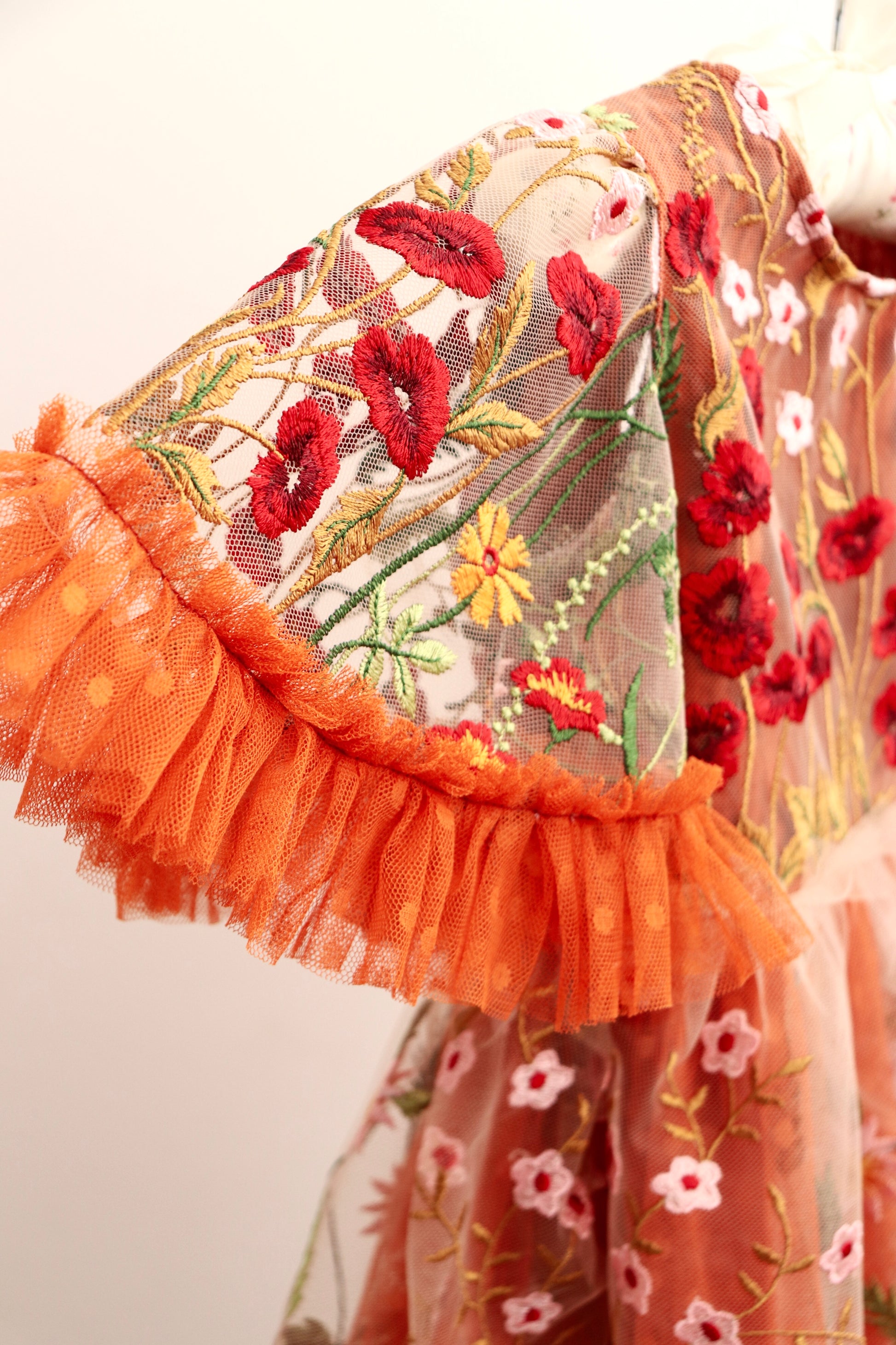 Close-up of girl embroidered photo prop dress featuring red and yellow floral embroidery with orange tulle ruffle sleeves