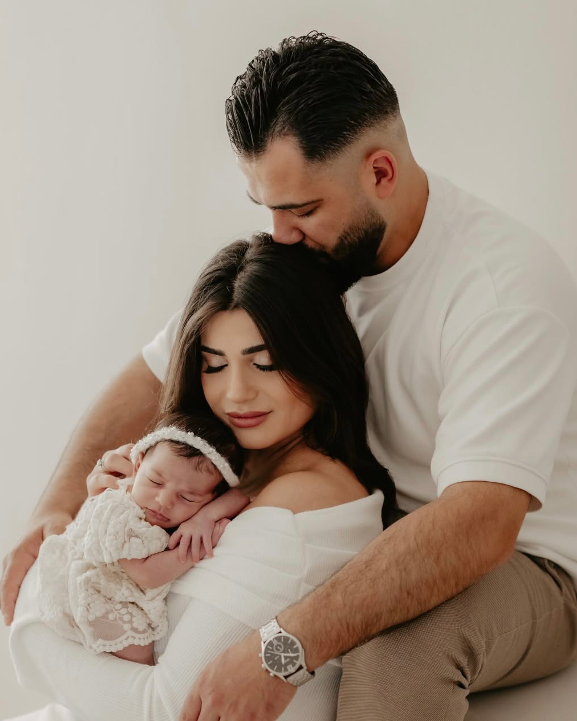 Newborn baby in lace newborn photo outfit held by mother with father embracing them both