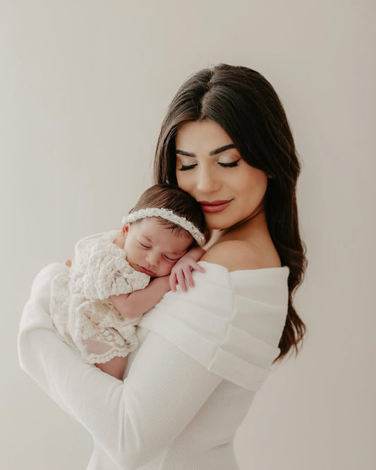 Newborn baby wearing lace newborn photo outfit and headband sleeping in mother's arms