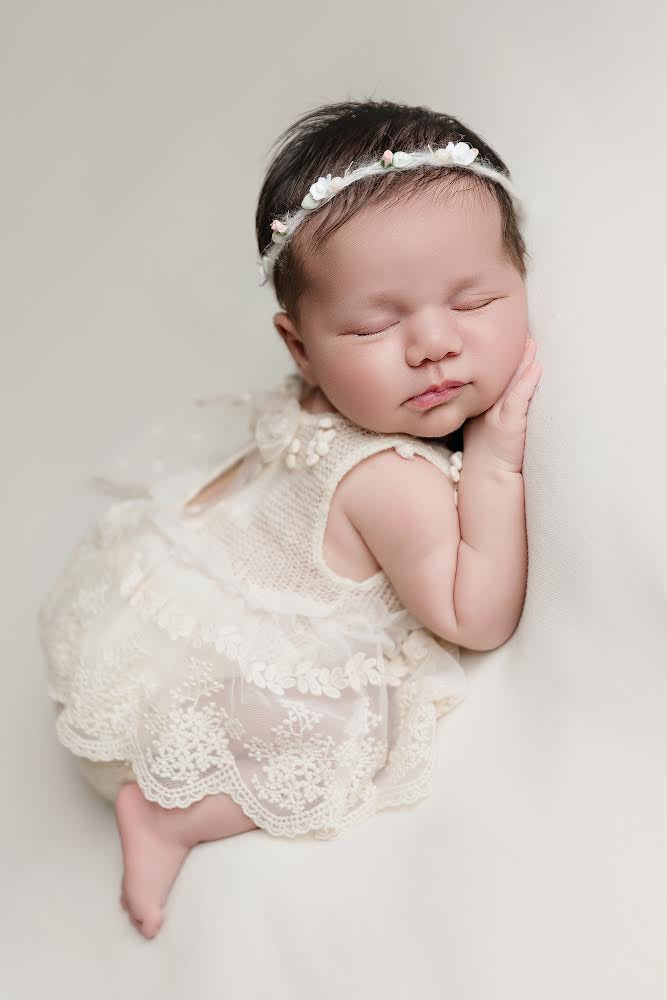 Sleeping baby wearing a delicate newborn lace romper outfit with floral headband on white background