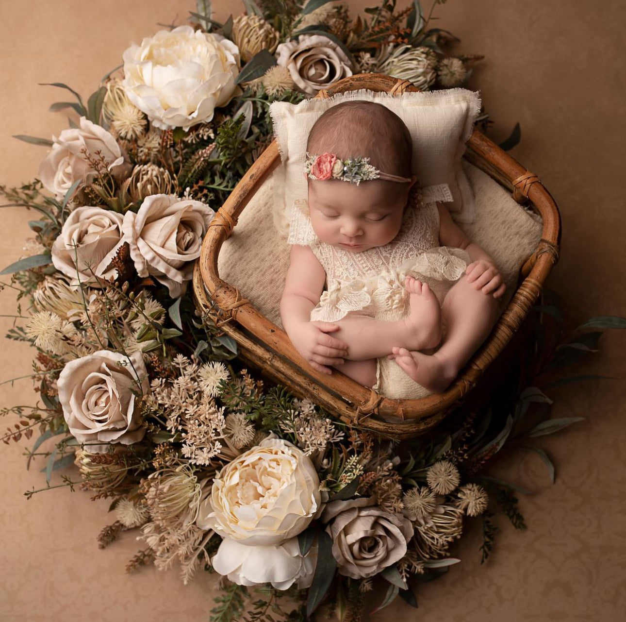 Newborn baby wearing a newborn photography prop dress by FLEUR MARGOT sleeping in a basket surrounded by soft floral decorations