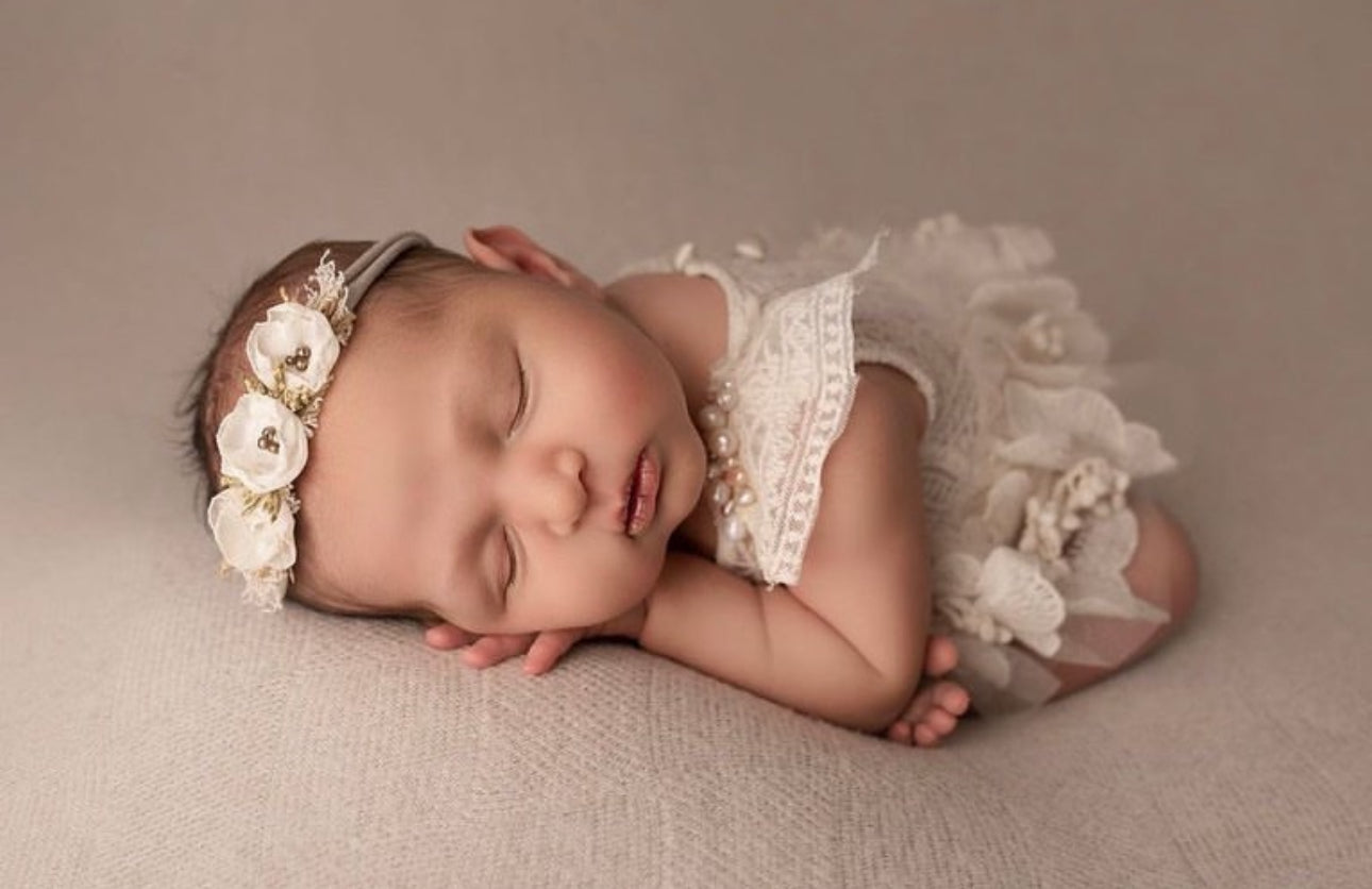 Newborn baby wearing white lace dress and floral headband as a newborn photography prop dress