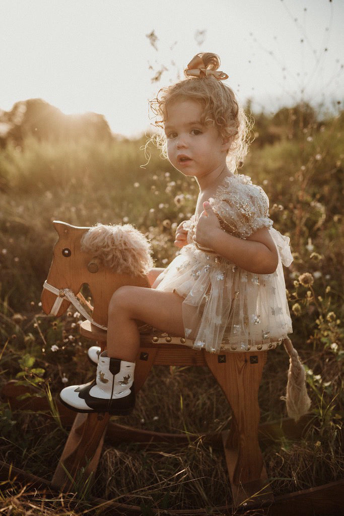 Girls wearing a floral photography prop dress for girls sitting on a wooden rocking horse outdoors