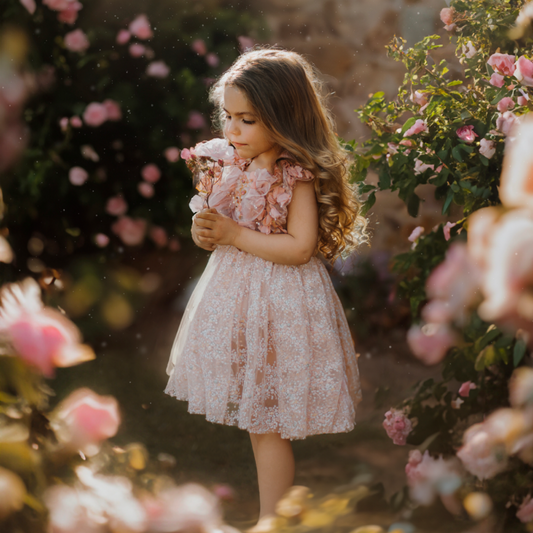 Young girl wearing a pink sitter session dress pink by FLEUR MARGOT holding a flower in a garden