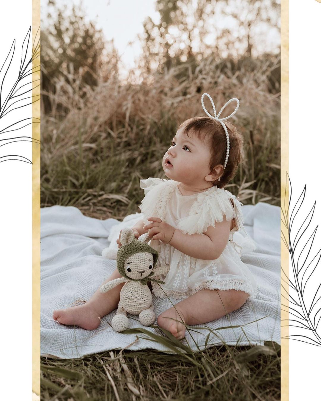 Baby wearing sitter session photography clothes sitting on blanket outdoors holding crochet toy