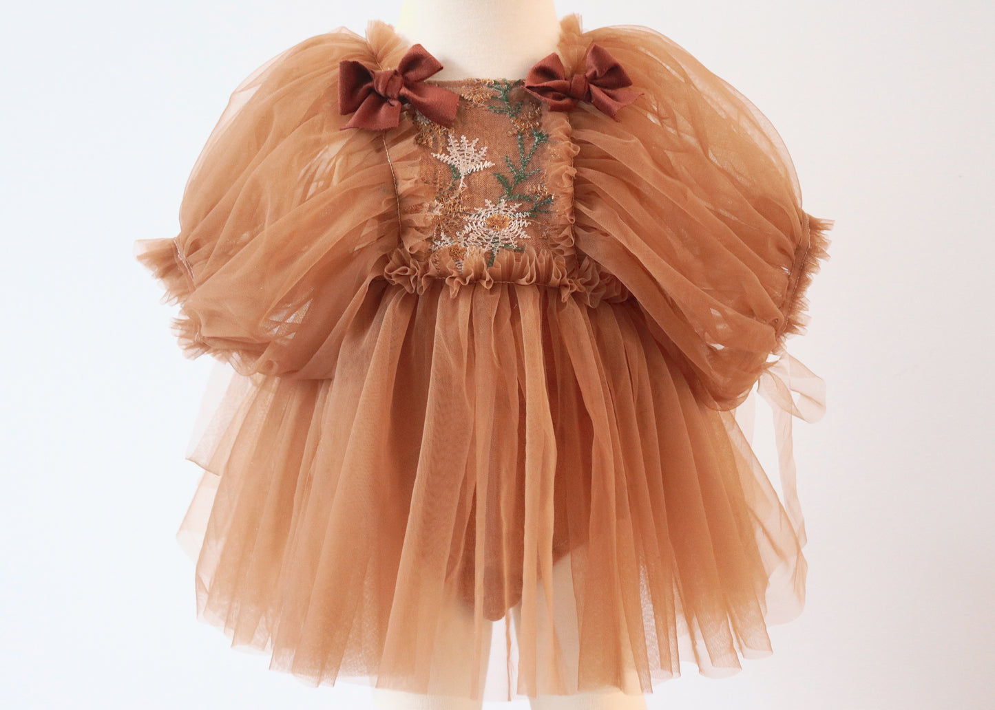 "Little girl in a soft brown tulle dress with puffy sleeves and brown velvet bows, standing in nature during a boho-style photoshoot."

