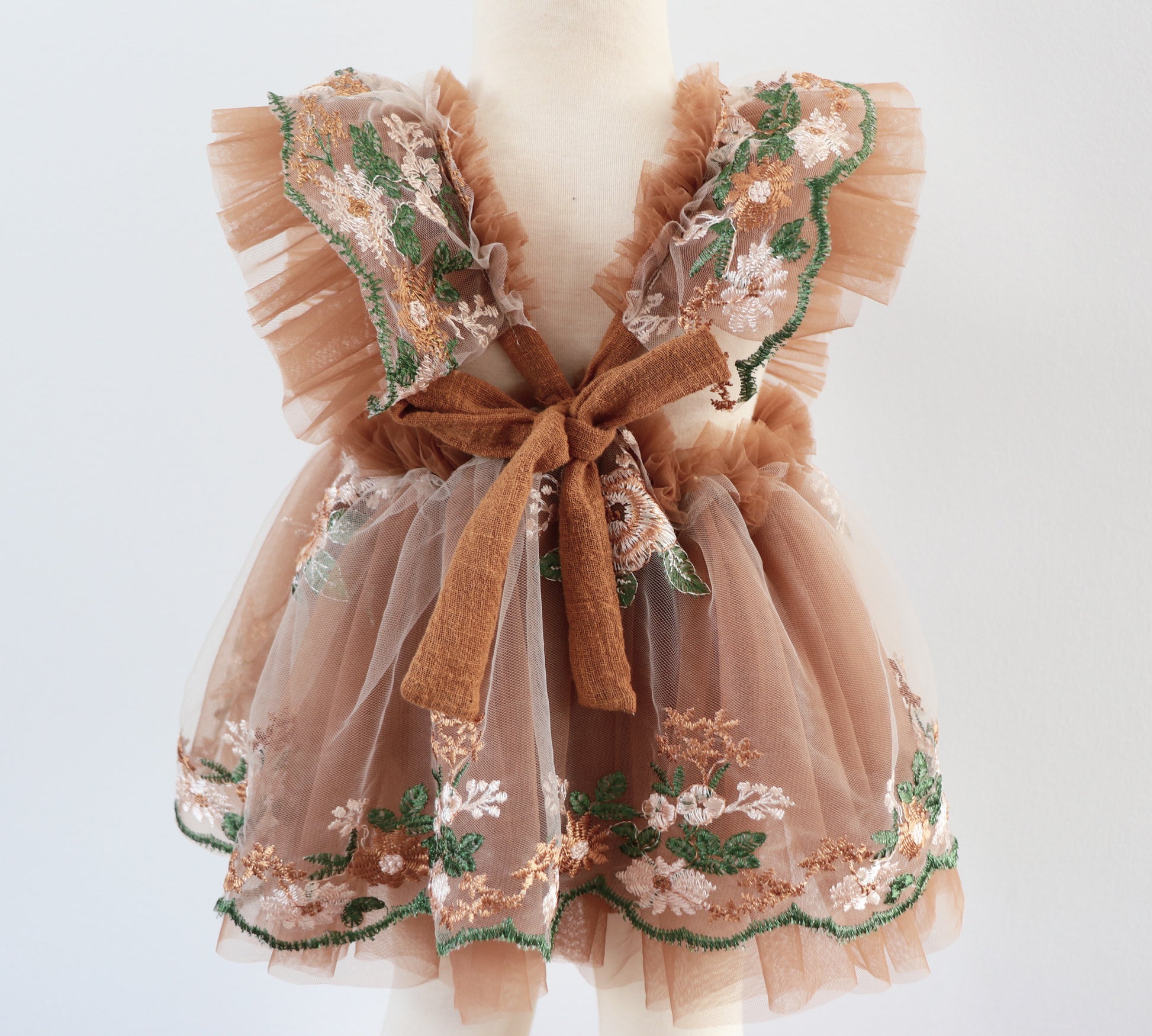 "Close-up of a girl's boho dress featuring warm-toned floral embroidery, ruffled details, and light brown tulle, styled for a birthday or outdoor shoot."

