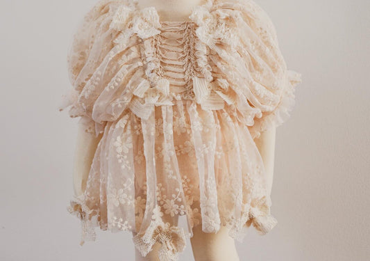 "Detail shot of embroidered puff sleeves and lace ribbons on a soft beige vintage dress for girls."

