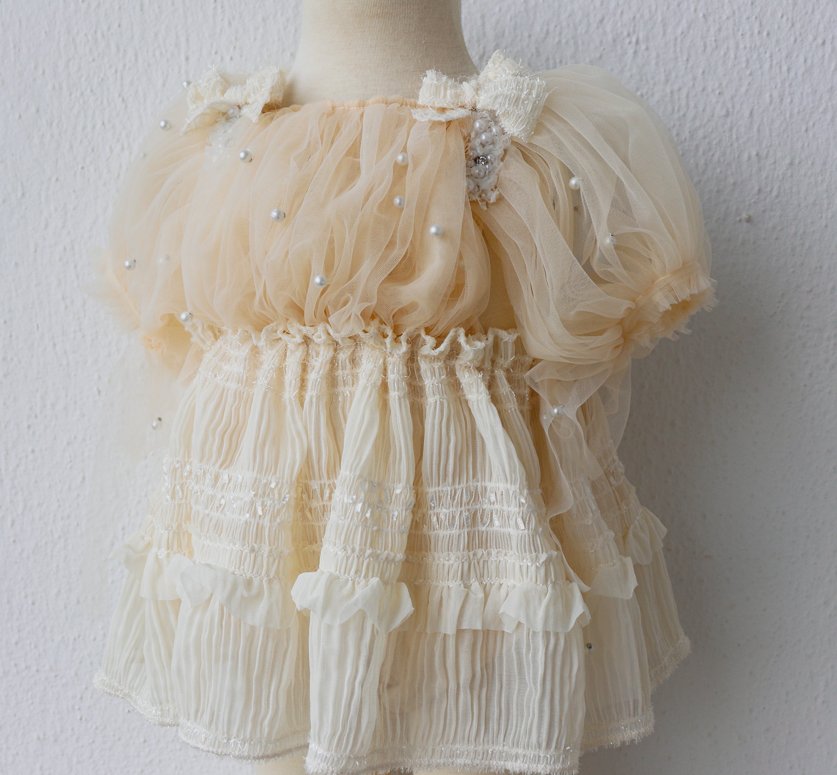 Close-up of baby romper with delicate pearl ruffles and ivory chiffon overlay, ideal for baby’s special celebration.

