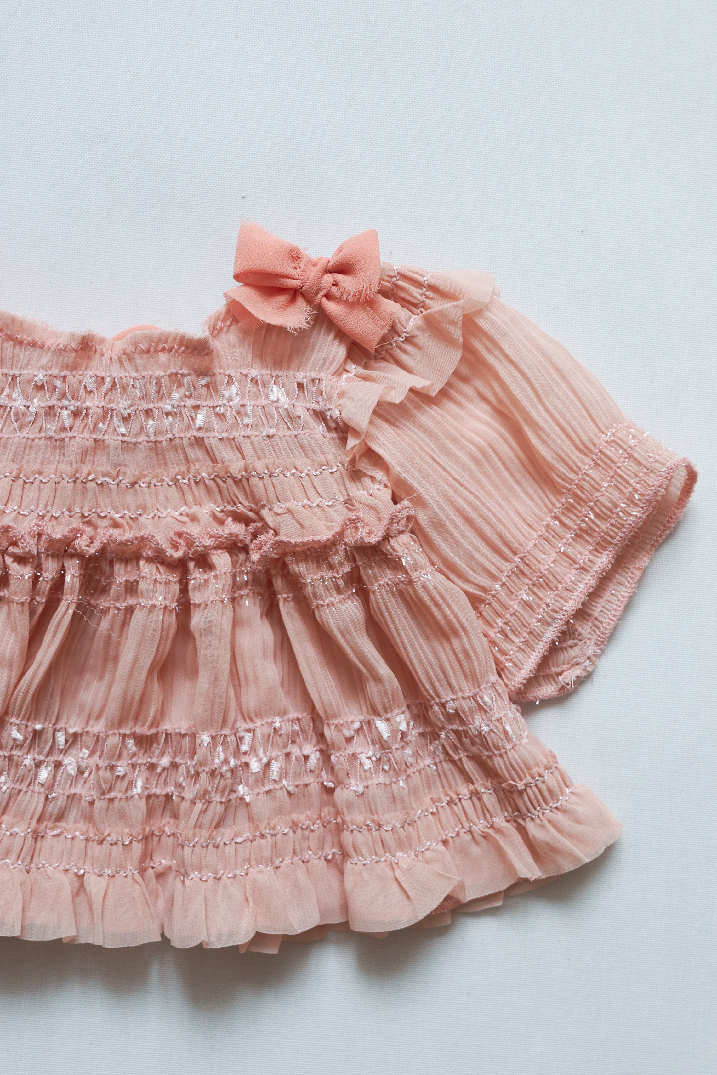 Beautiful dust pink newborn dress made from wrinkled chiffon, designed with long sleeves, delicate bows on the bodice, and a matching diaper cover for a cozy and elegant look during a newborn session.