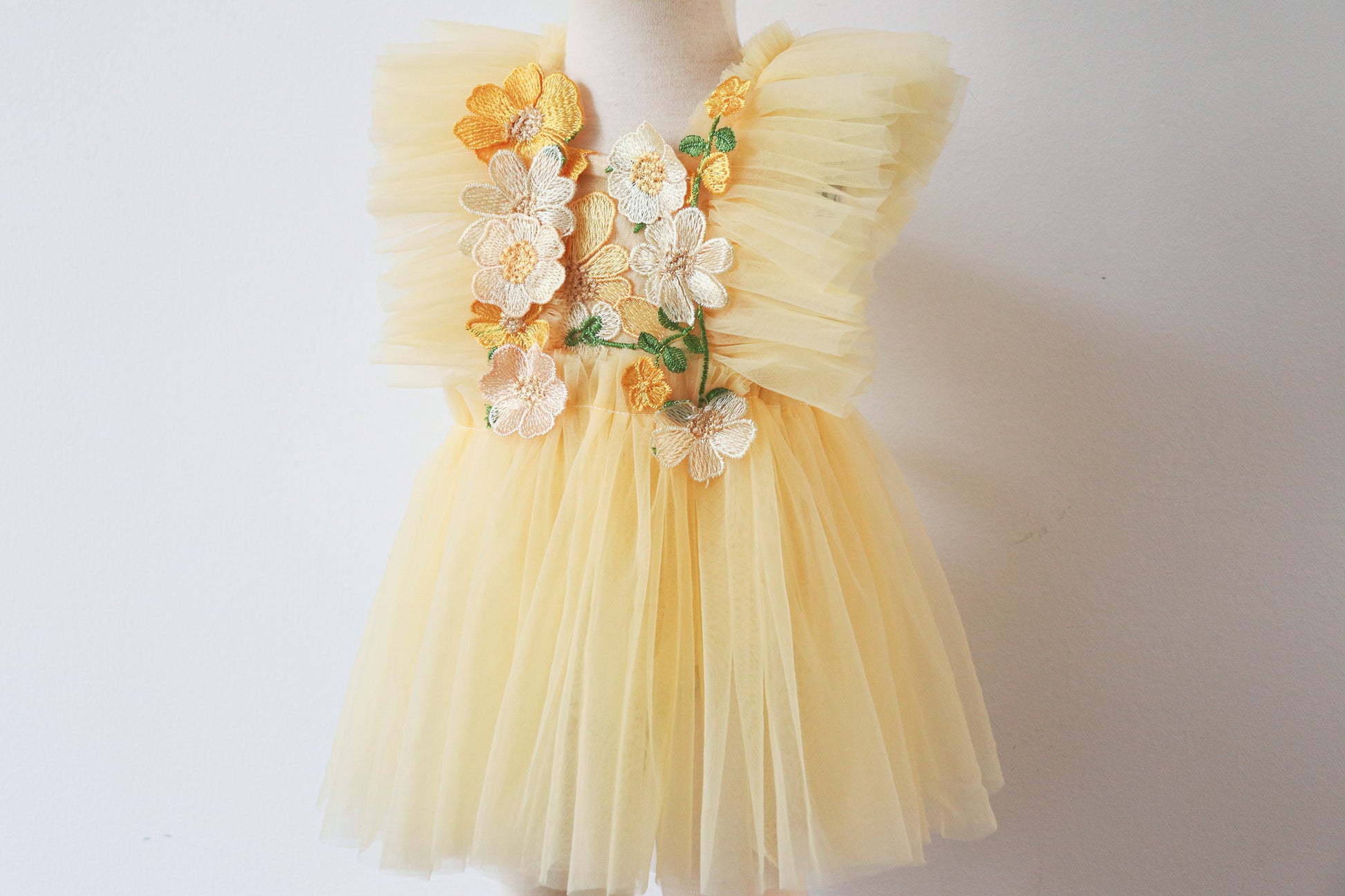 Soft yellow cotton girls' playsuit with delicate floral details and airy tulle, styled for a magical spring garden setting, evoking the charm of a flower fairy