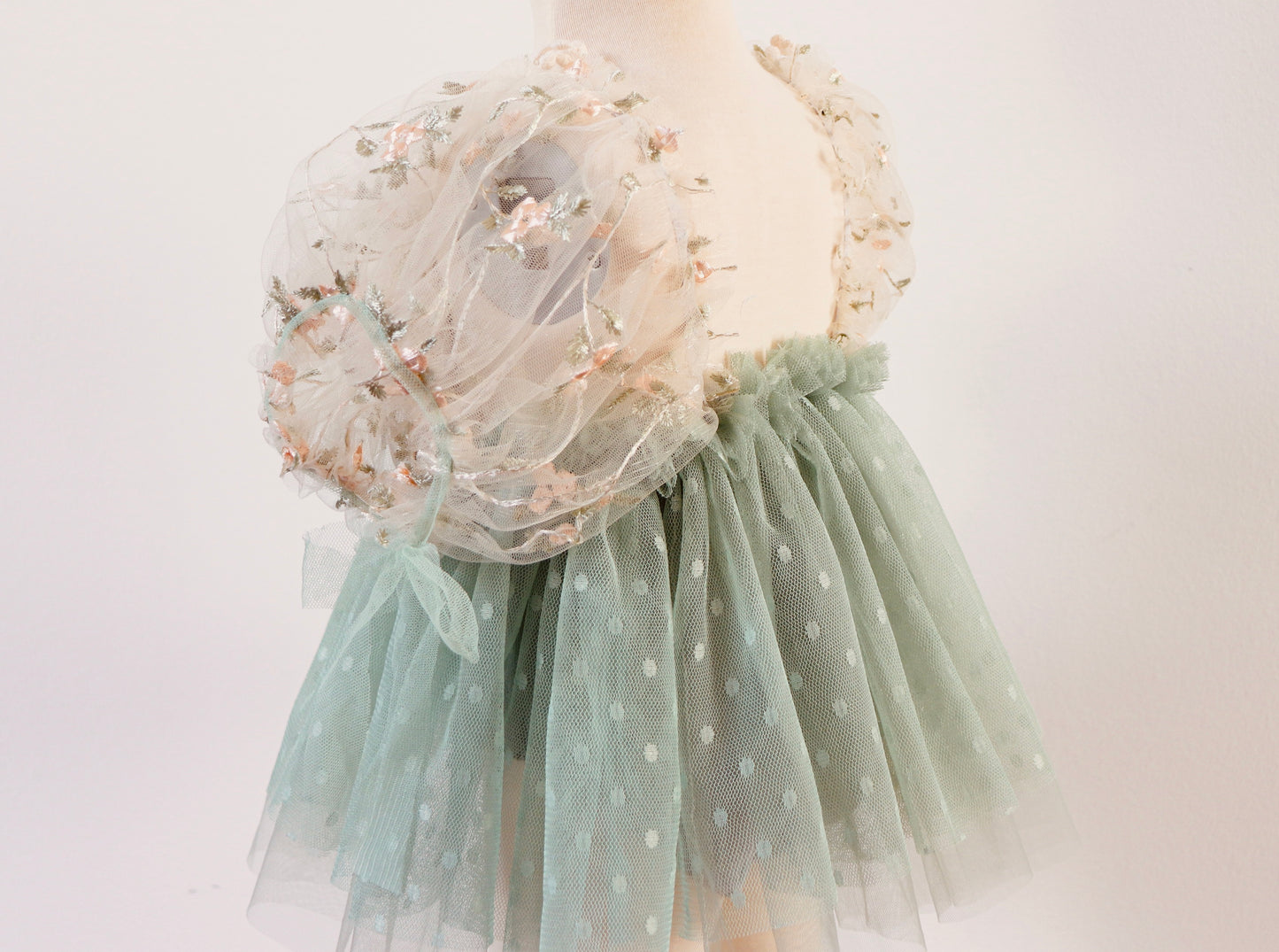 "Little girl twirling in a sage green fairy-style dress with puffy tulle sleeves and a vintage lace bodice during a garden photoshoot."

