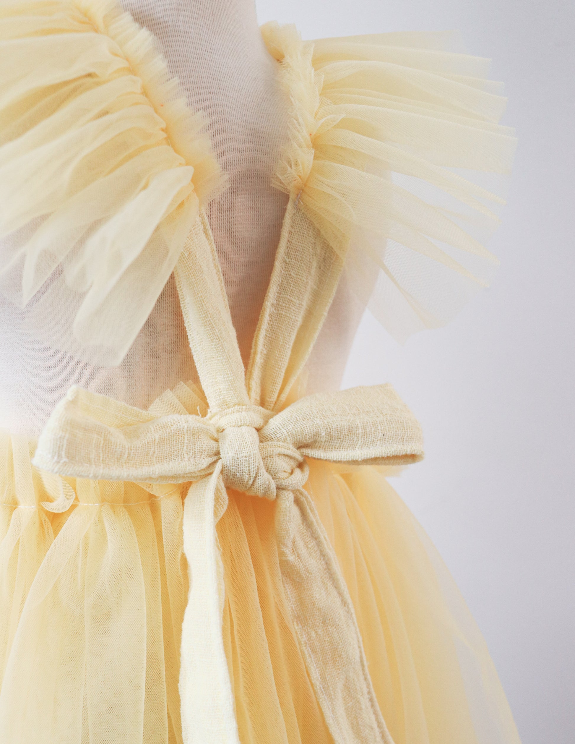 A little girl twirling in a fairy-inspired yellow playsuit dress, with fluttering tulle ruffles and embroidered flowers, ideal for Easter celebrations and outdoor photoshoots