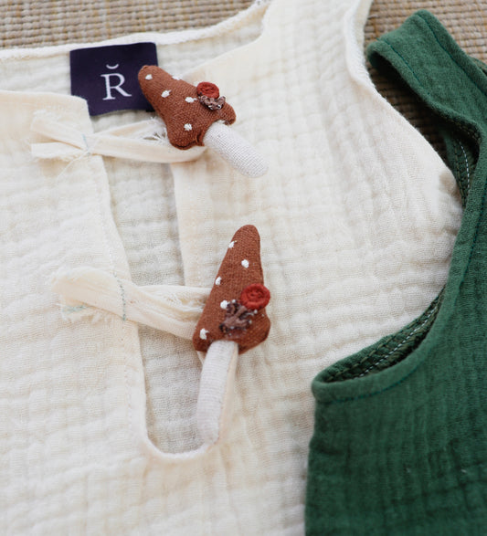 Baby boy sitting outdoors wearing a cotton gauze romper with mushroom buttons in ivory, perfect for nature-inspired photo sessions.

