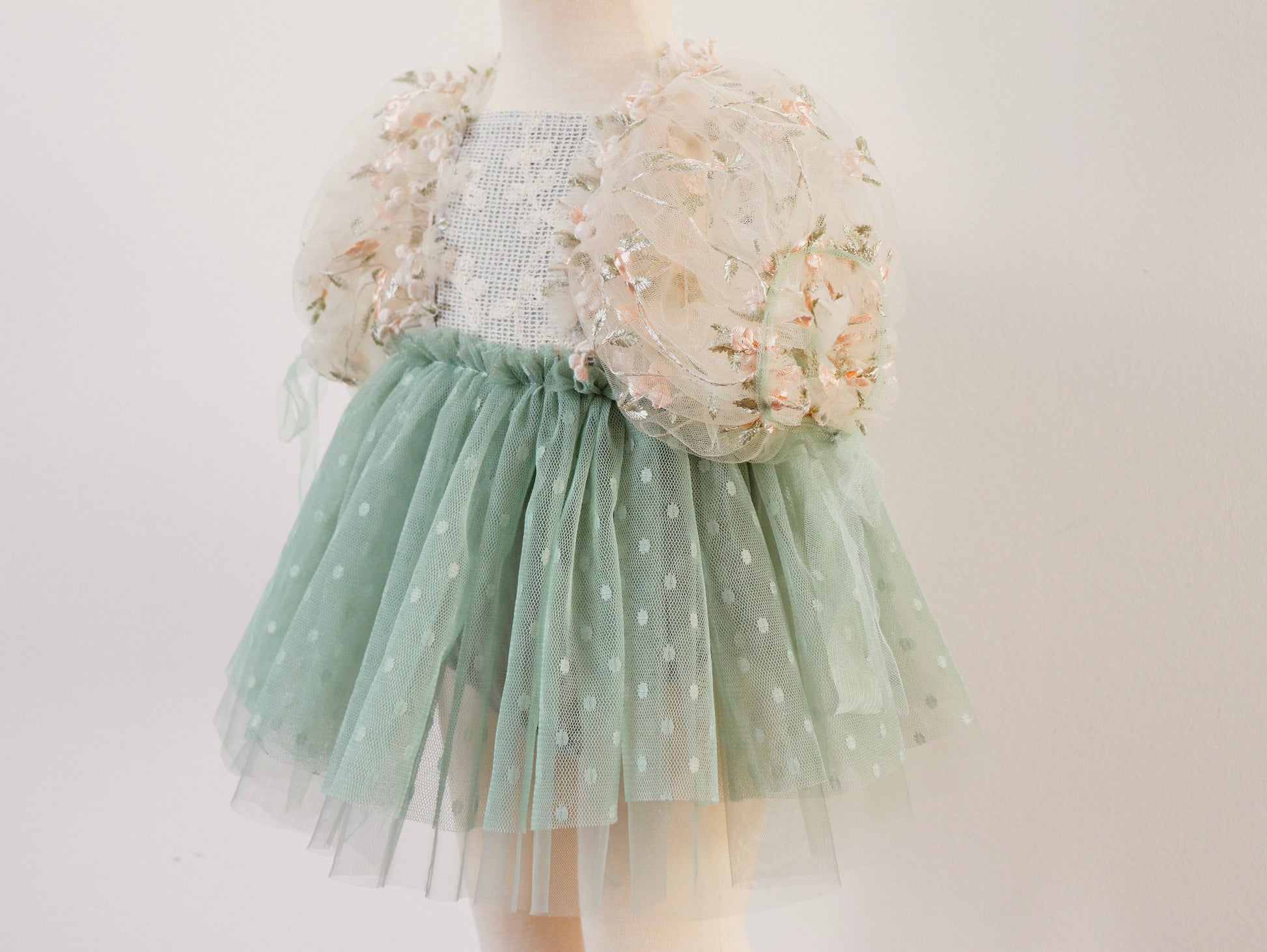 "Close-up of a green sage dress with embroidered flowers and vintage lace details, styled in a classic overall silhouette for girls."

