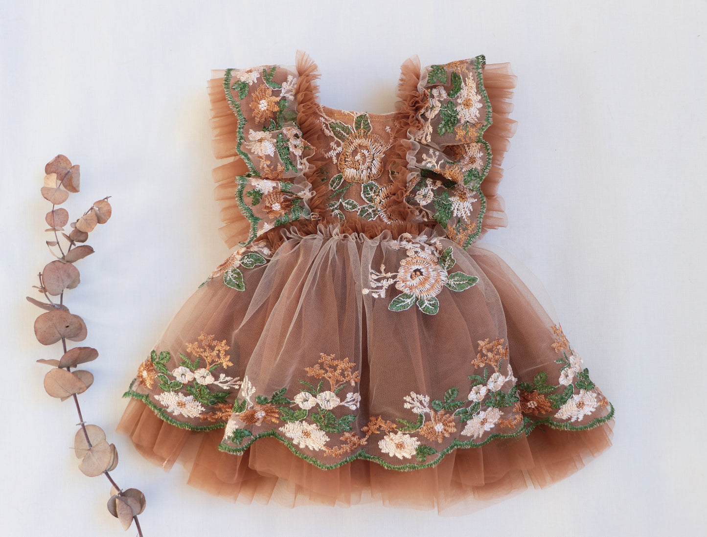 "Little girl wearing a soft brown tulle dress with floral embroidery and ruffled bodice, posing in an outdoor boho-inspired photo session."

