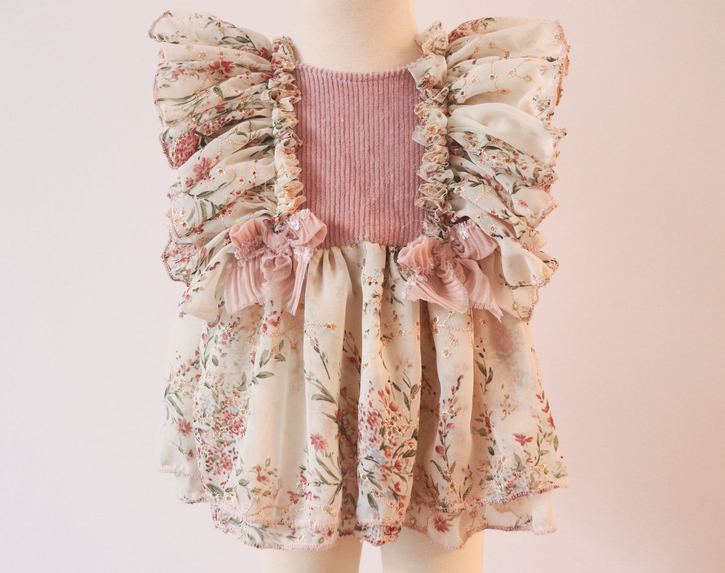 Close-up of a pink velvet and floral chiffon dress for little girls, showcasing ruffled shoulders, double chiffon skirt, and delicate bow details with matching diaper cover.