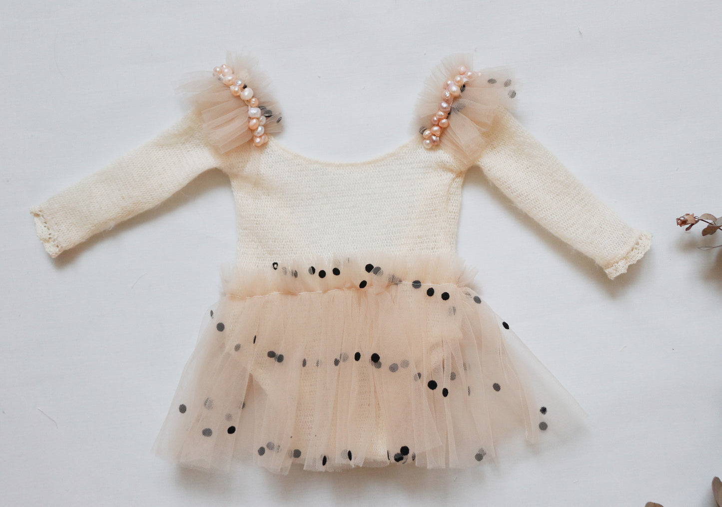 Close-up of a skirt-style newborn romper showcasing ruffled black-dotted tulle and freshwater pearls.