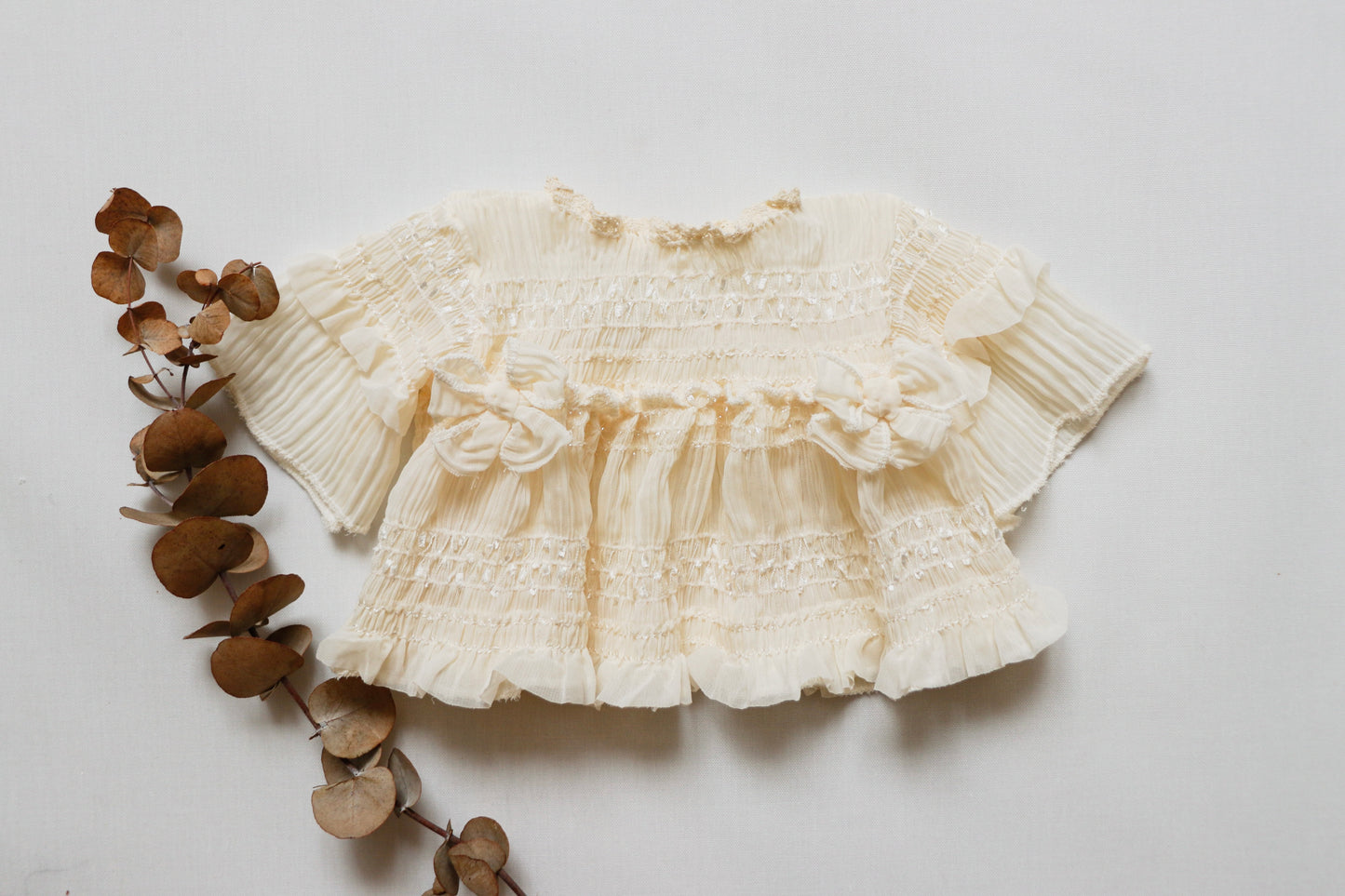 Newborn girl dress in soft ivory wrinkled chiffon fabric, featuring long sleeves, a matching diaper cover, and two delicate bows on the bodice, perfect for photoshoots and newborn sessions."