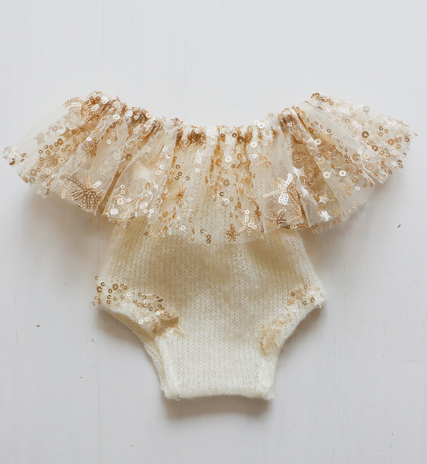 Soft cream newborn romper with a ruffled neck and golden embroidered stars, perfect for a festive photoshoot.