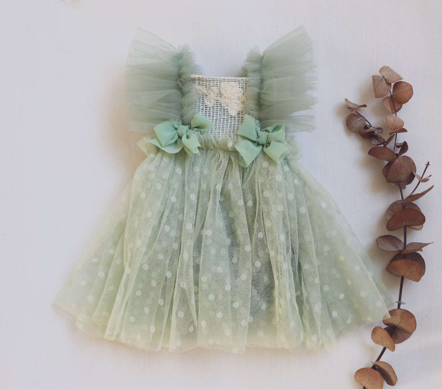 "Newborn baby girl in a sage green dress with vintage lace bodice, ruffled tulle sides, and crossed tulle straps – styled for a soft, fresh newborn session."

