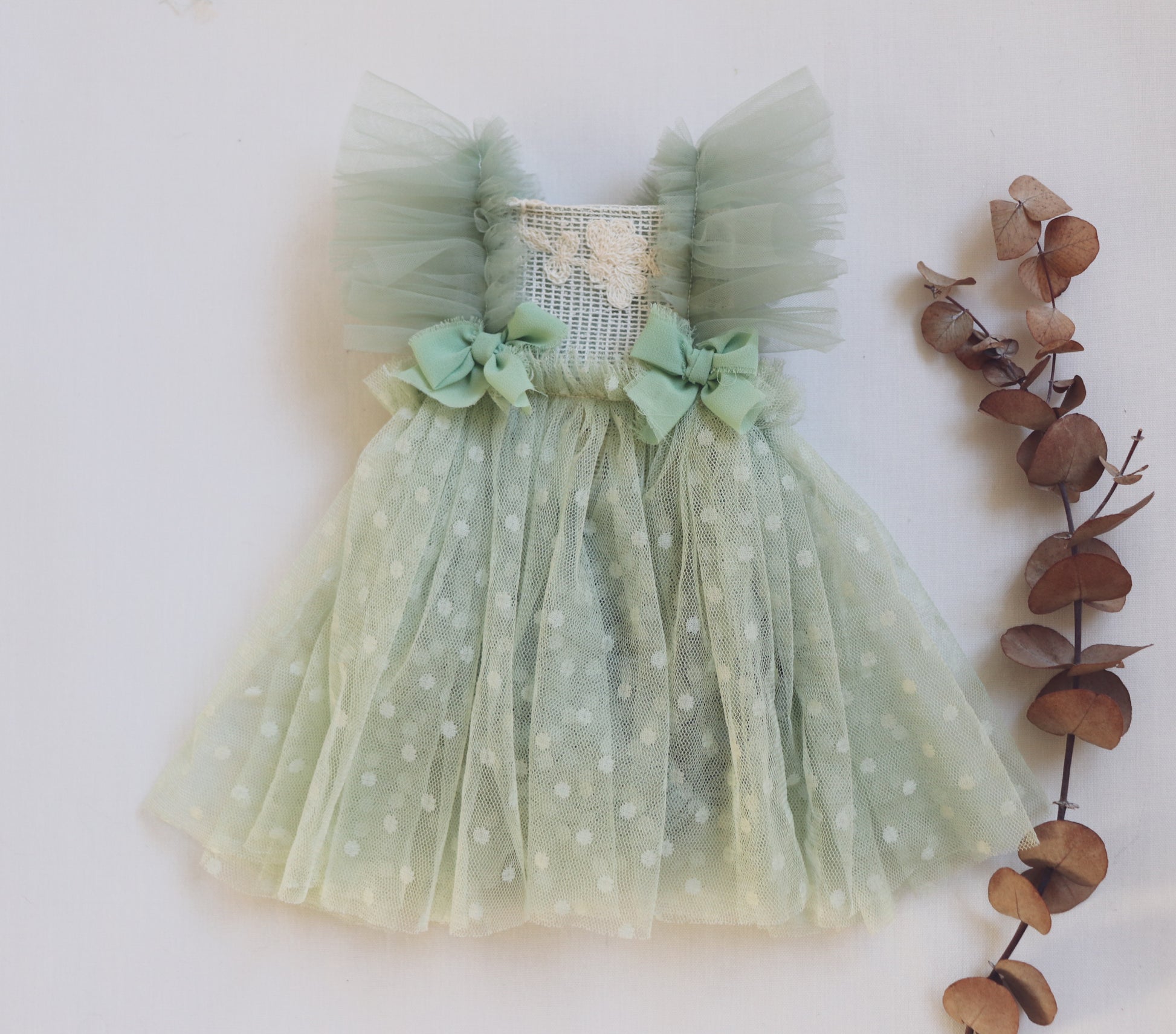 "Newborn baby girl in a sage green dress with vintage lace bodice, ruffled tulle sides, and crossed tulle straps – styled for a soft, fresh newborn session."

