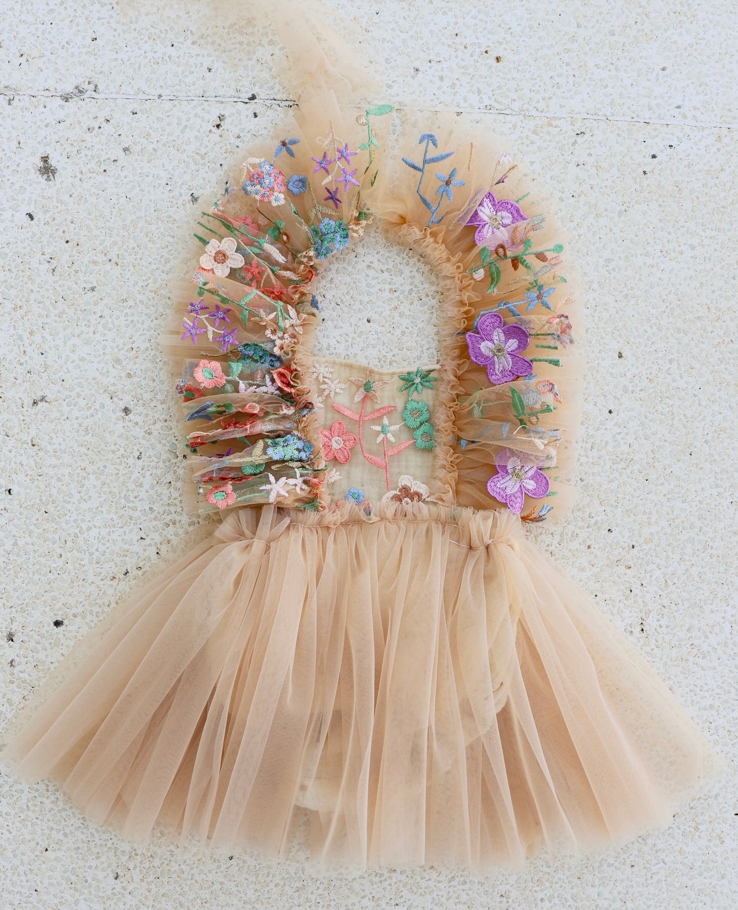 Little girl walking through a meadow in a nude tulle dress with ruffled shoulders and embroidered floral bodice, perfect for a spring photo session.

