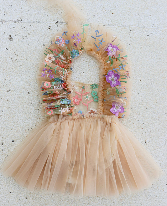 Little girl walking through a meadow in a nude tulle dress with ruffled shoulders and embroidered floral bodice, perfect for a spring photo session.


