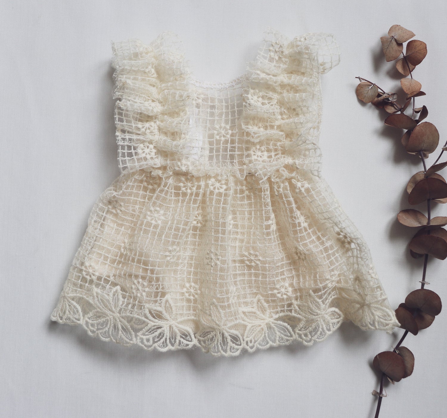 "Newborn baby girl wearing a soft light beige romper with embroidered lace and tiny flowers, peacefully posed during a natural light photo session."

