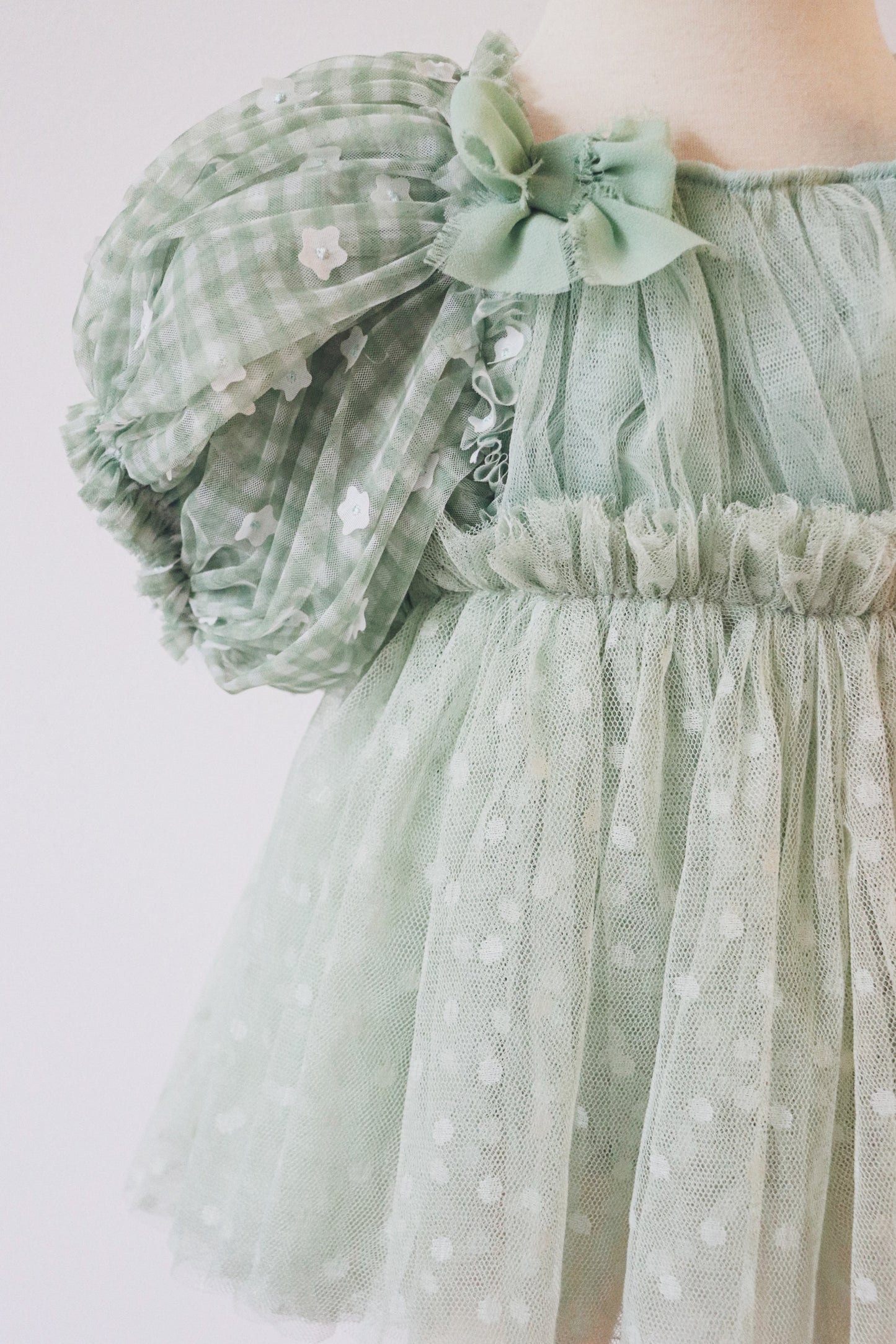 A sweet soft green pastel girls' dress with crossed adjustable straps, puffy sleeves adorned with white flowers, perfect for birthday parties and outdoor photoshoots.