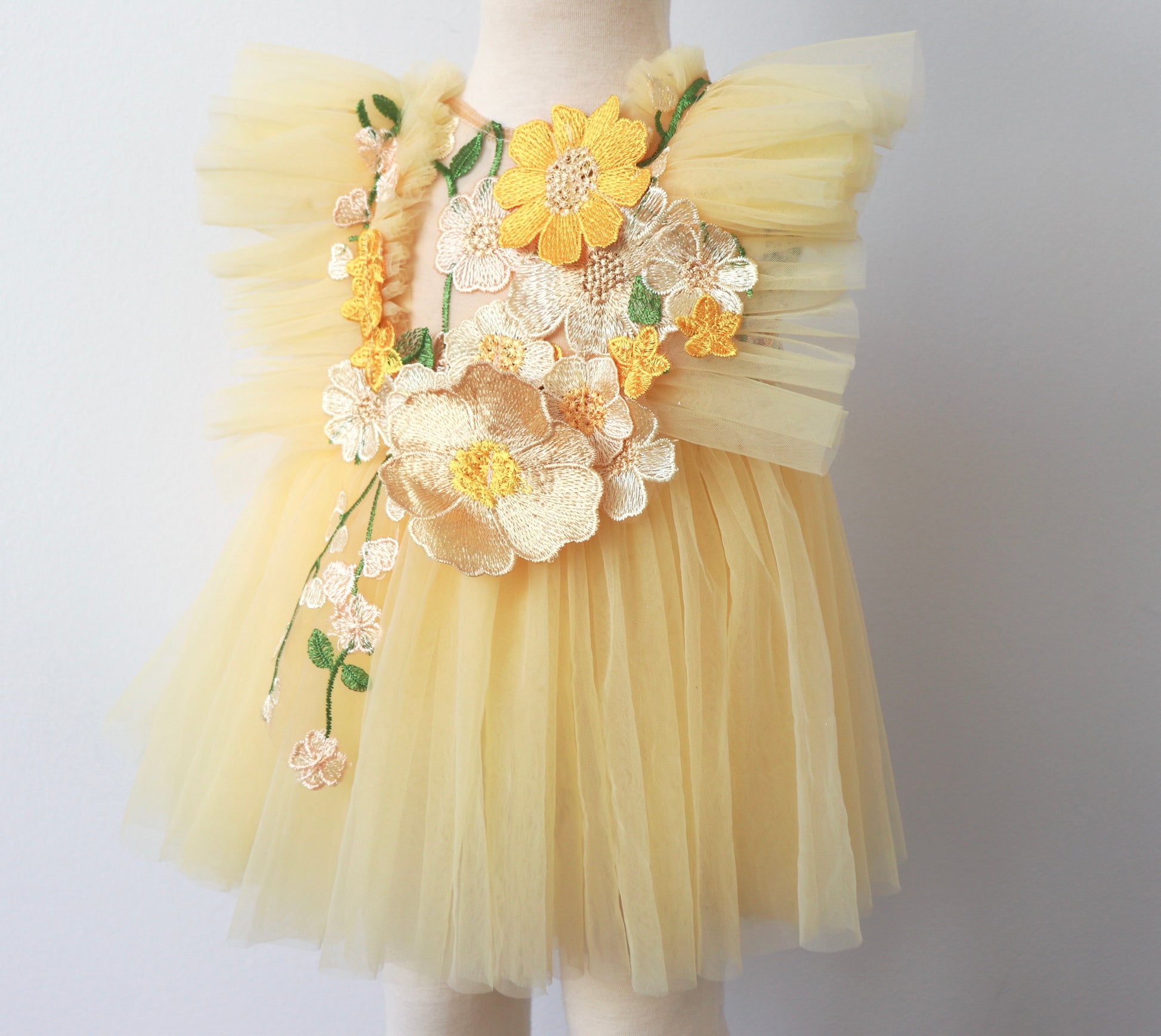 "Close-up of a girl's yellow tulle dress with delicate summer flower embroidery and matching bloomer, styled for a garden party or birthday."

