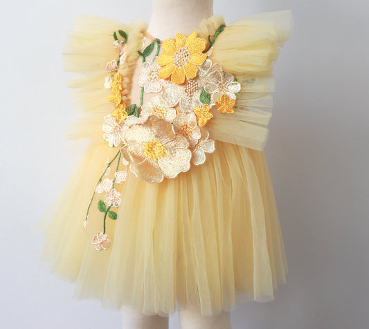 "Close-up of a girl's yellow tulle dress with delicate summer flower embroidery and matching bloomer, styled for a garden party or birthday."

