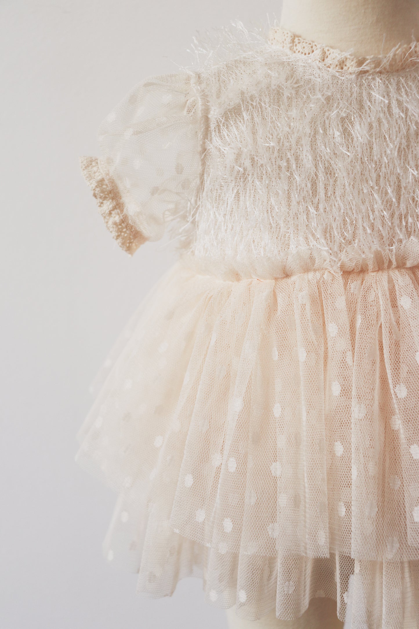 Toddler girl wearing a two-piece outfit with ivory fringe feather bodice and layered beige dotted skirt in a photoshoot setting."
