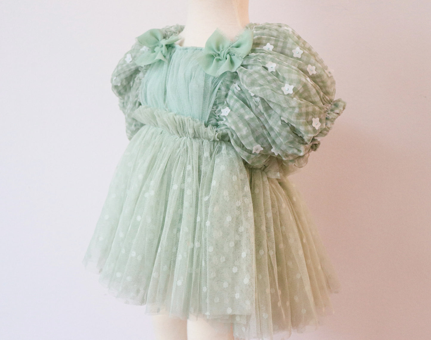 Little girl wearing a soft green pastel dress with crossed straps and puffy floral sleeves, capturing the elegance and charm of spring and summer celebrations.