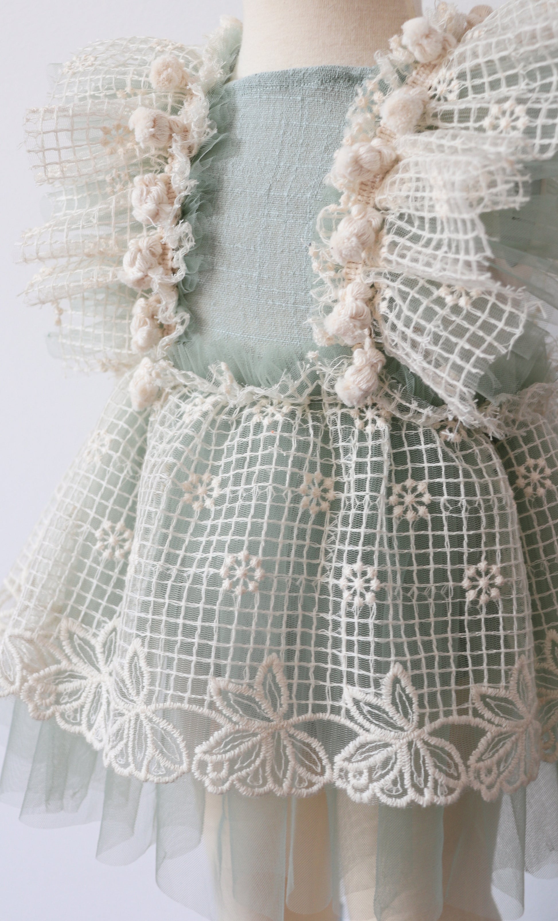 Sage green vintage-inspired girls' playsuit with ruffled lace and tulle details, adjustable crossed straps, and bohemian beige fringes, perfect for photoshoots and special occasions