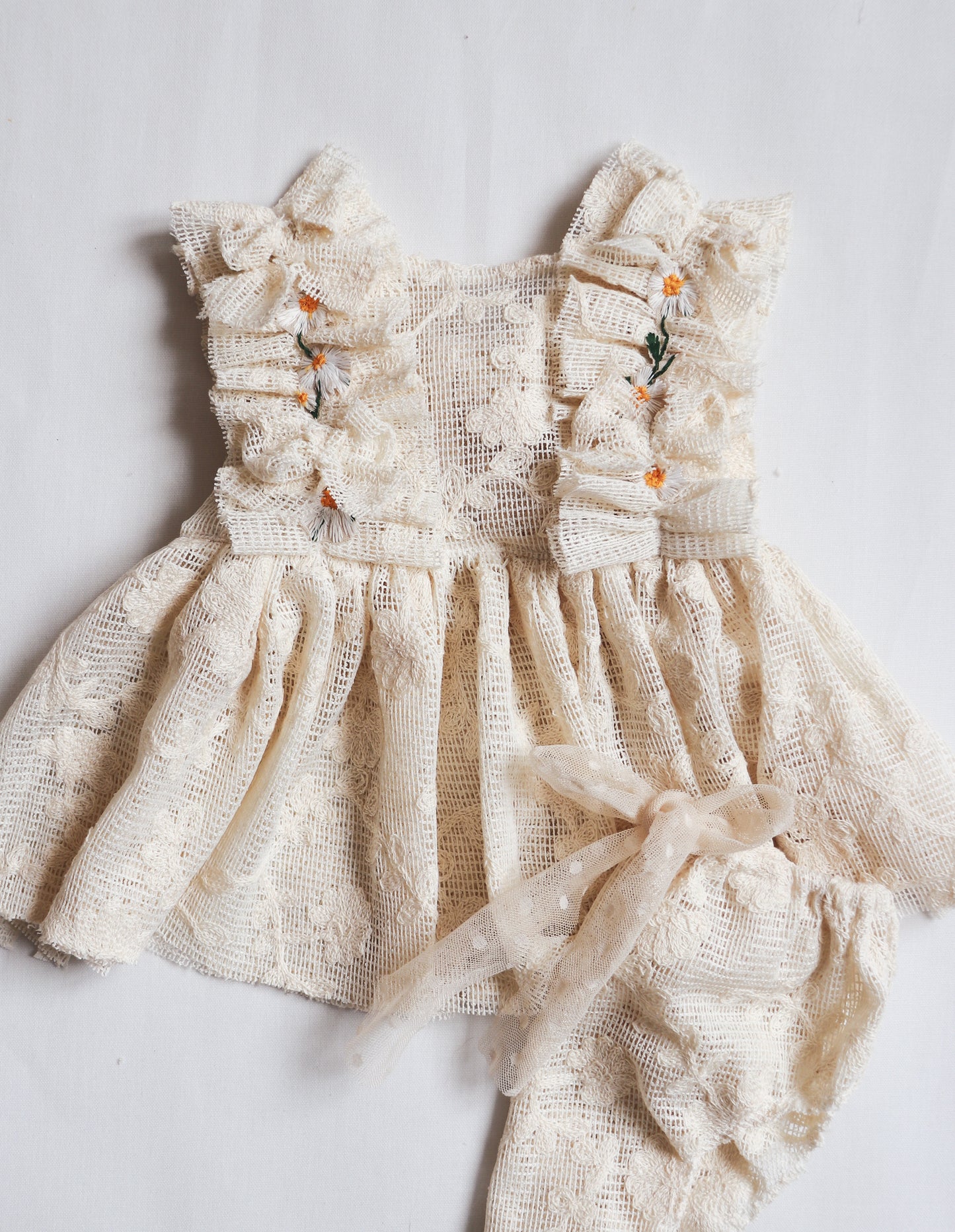 "Close-up of a girl's dress featuring delicate vintage lace, daisy appliqués, and mini bows on the bodice, styled for a bohemian photo session."


