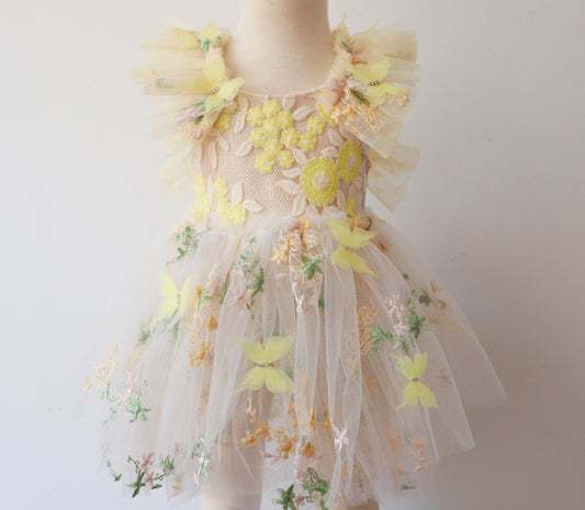 A charming girl's dress featuring delicate yellow floral embroidery and layered tulle with whimsical butterfly accents, ideal for Easter and springtime festivities.

