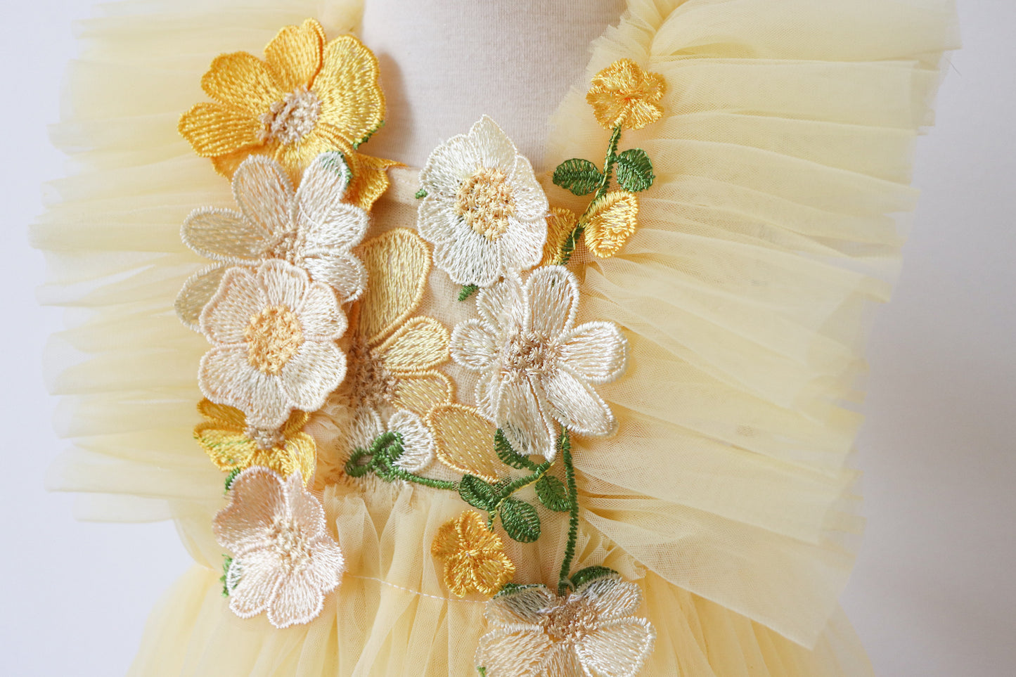 Close-up of a charming yellow playsuit for girls, featuring embroidered flowers on the bodice, soft tulle ruffles, and a classic overall silhouette, perfect for springtime adventures